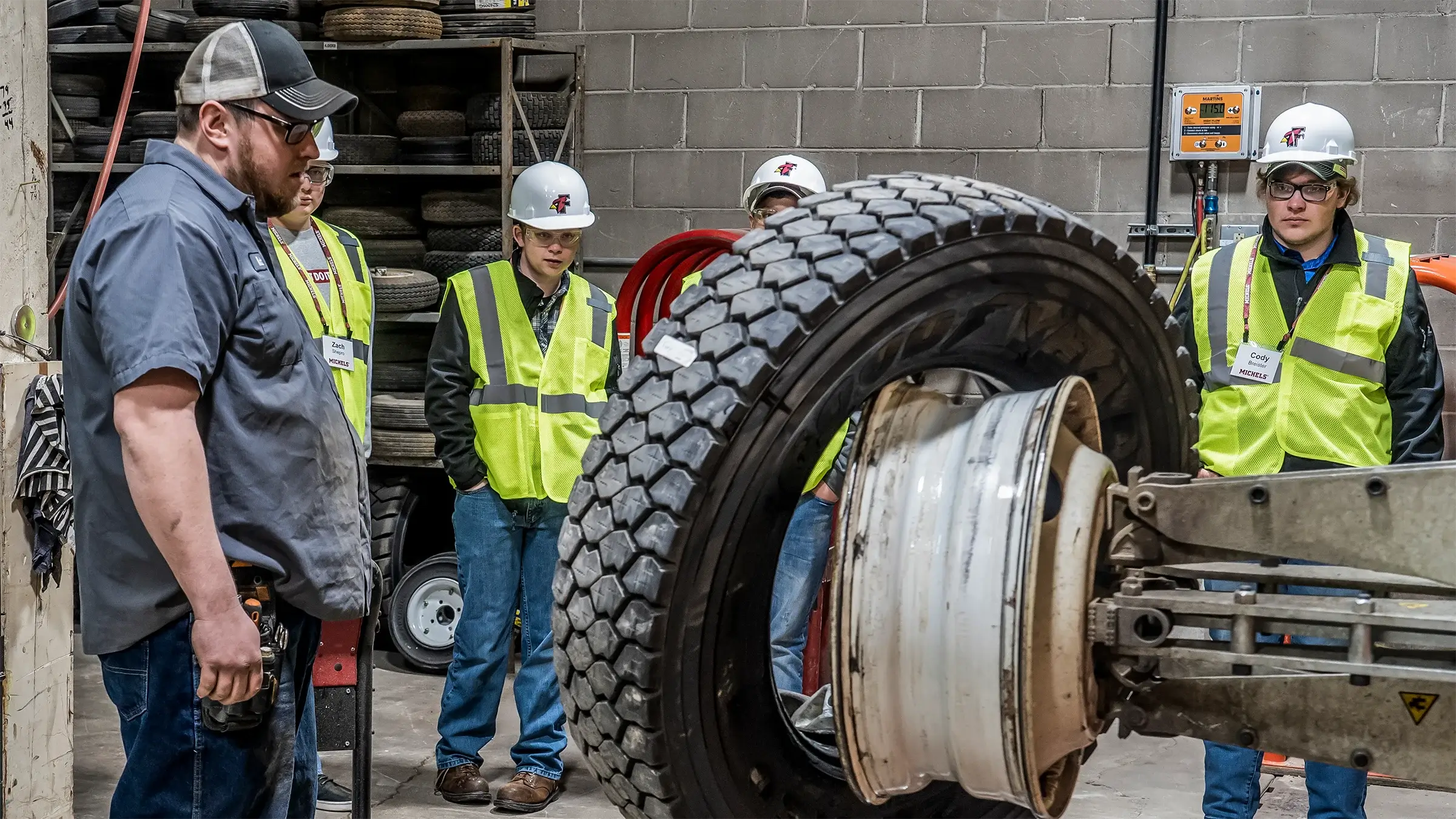 A mechanic shows students how a machine is used to change a tire in a tire shop.