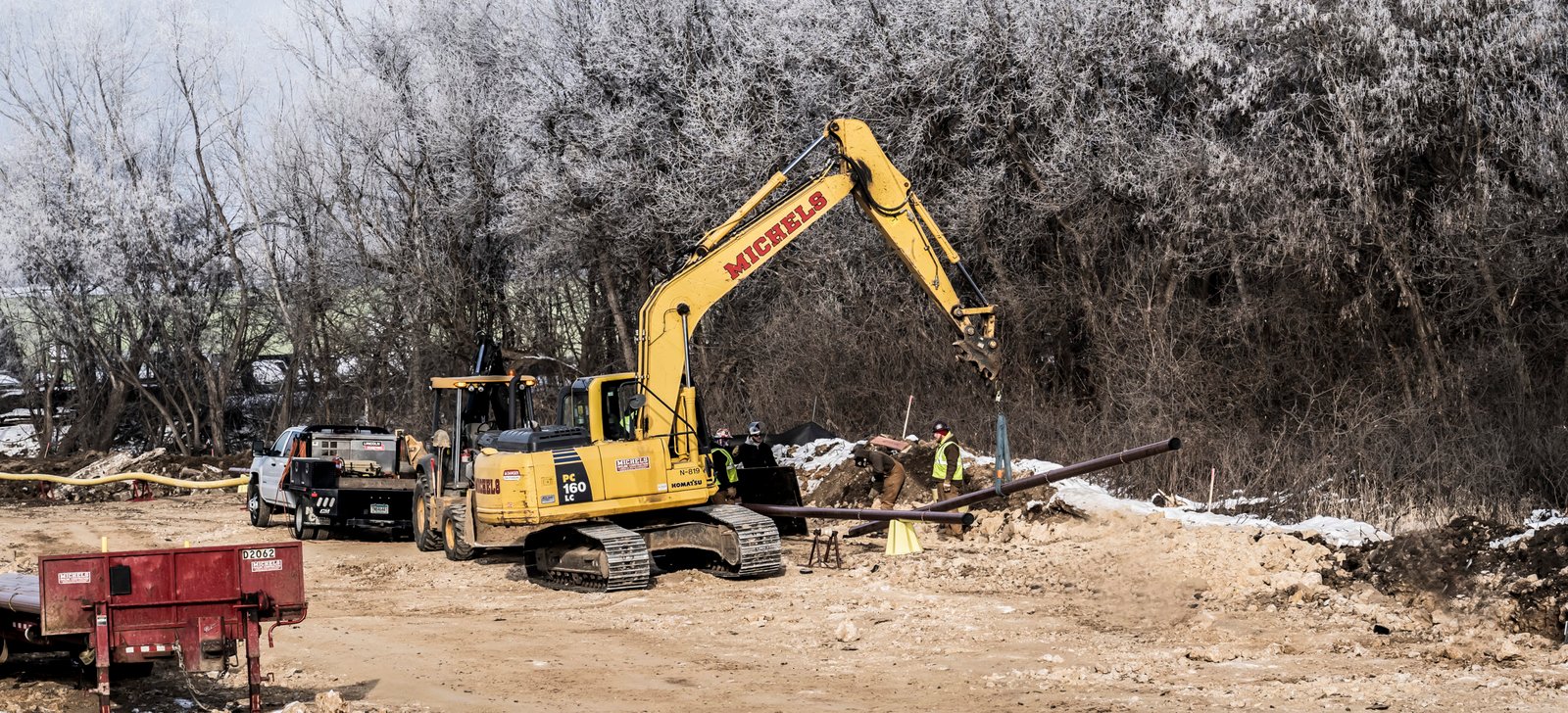 Excavator carries pipe into place on a winter day
