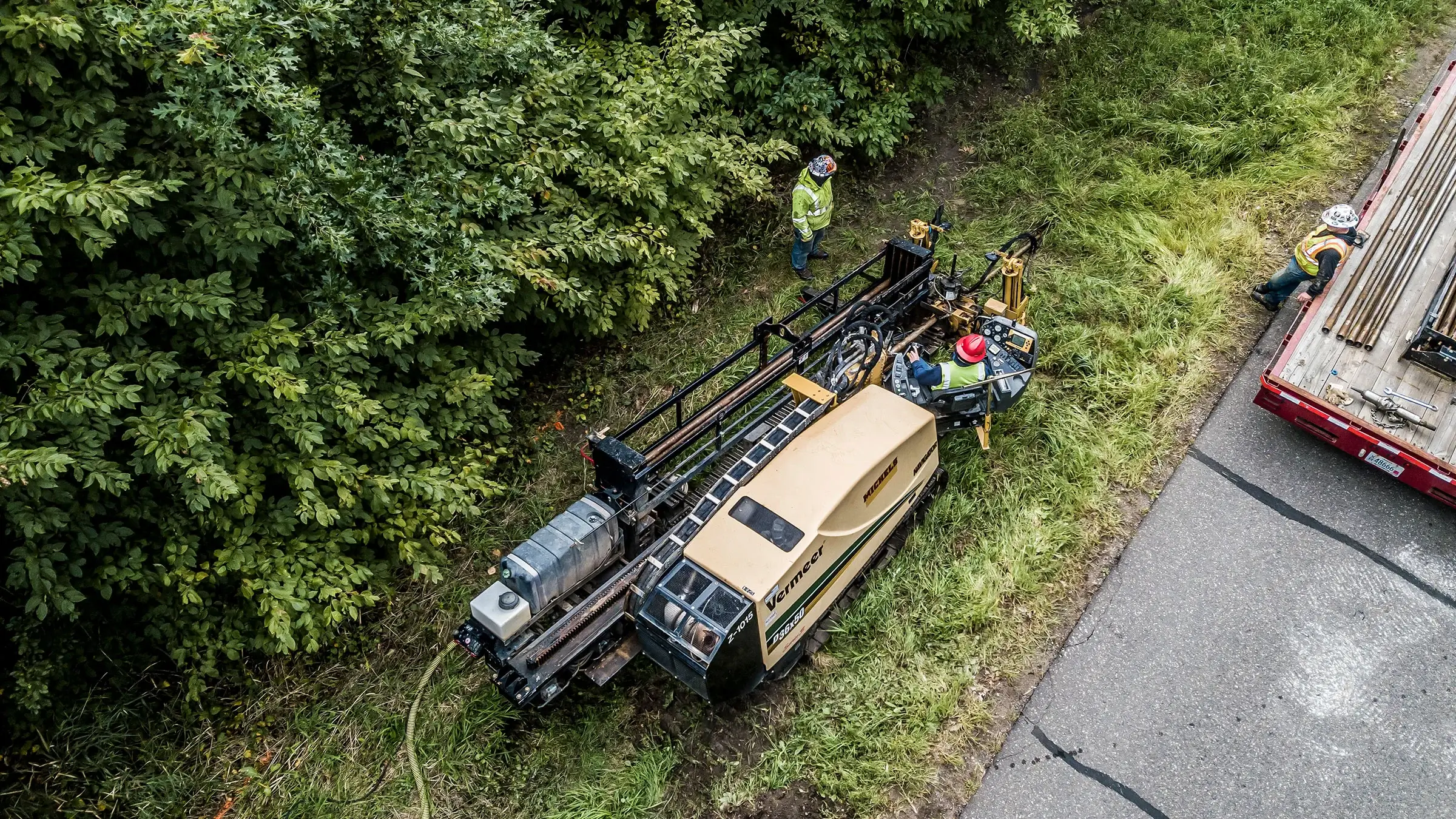 A small directional drill installs utility pipe near a roadside forest