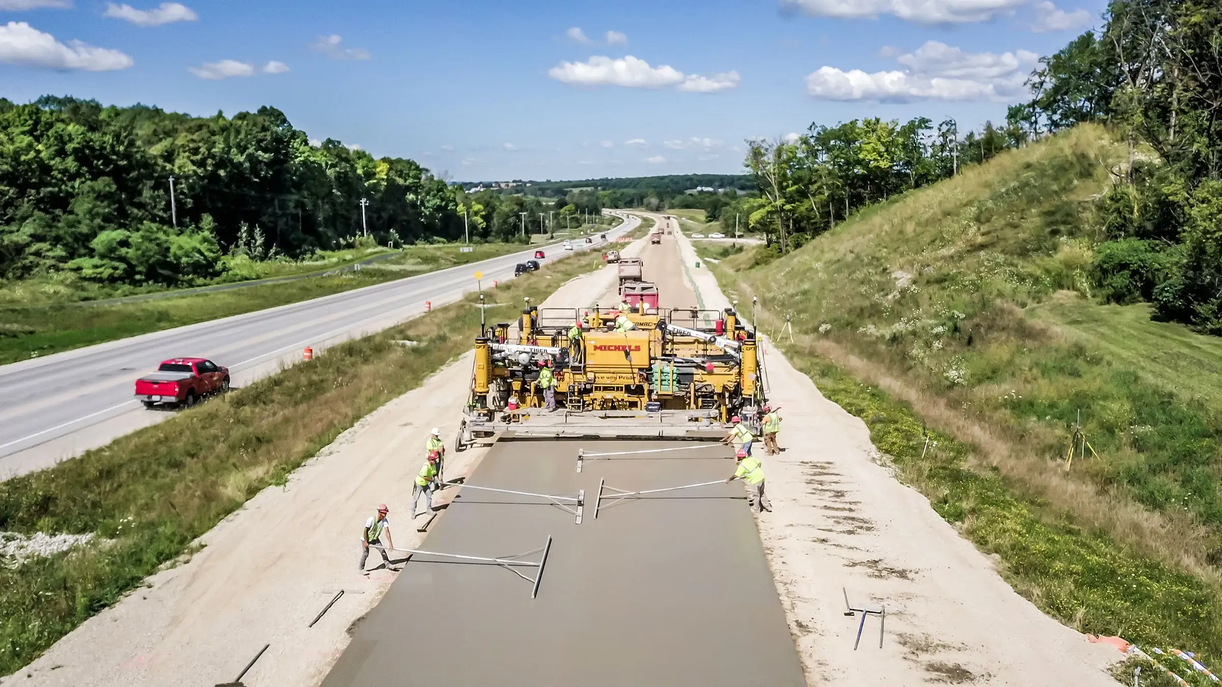 A concrete paving machine operates down a long stretch of highway.
