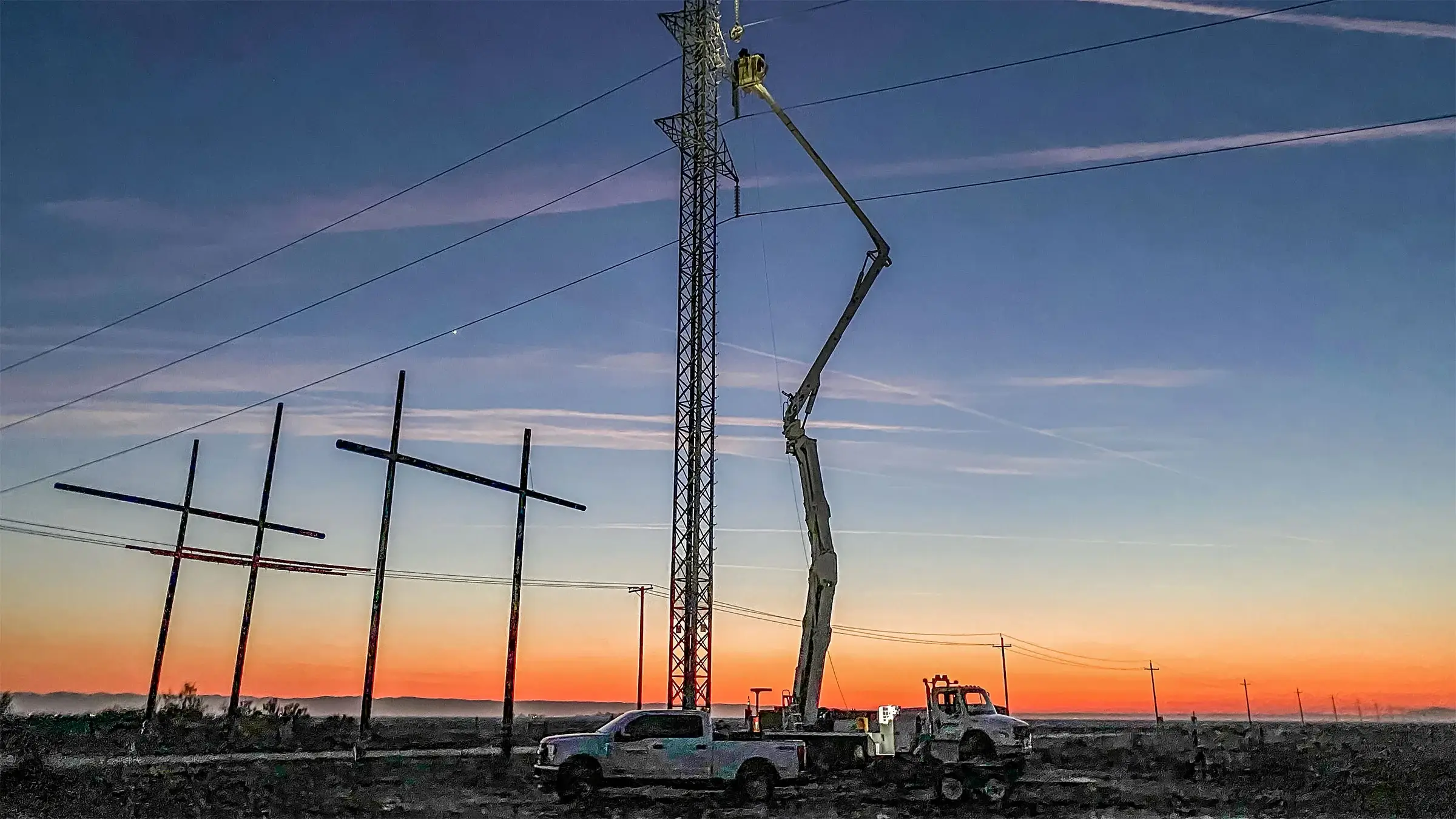 Lineworker works in a bucket truck against a dramatic sunset