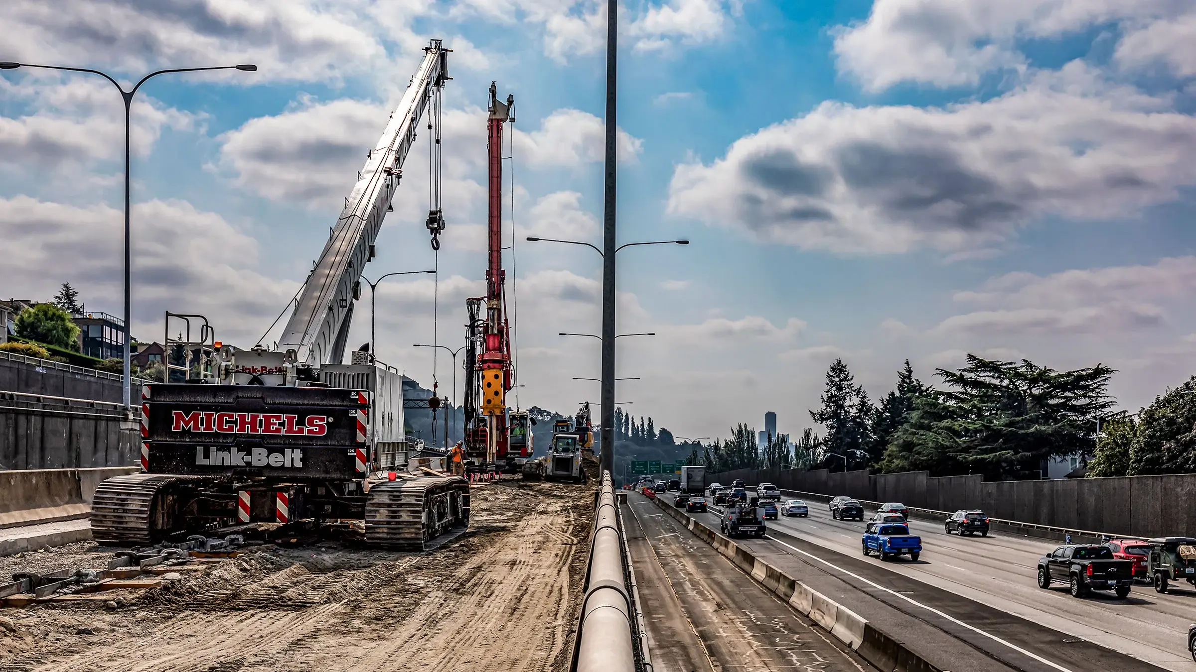A large crane and drill rig operate near a busy interstate outside of Portland.