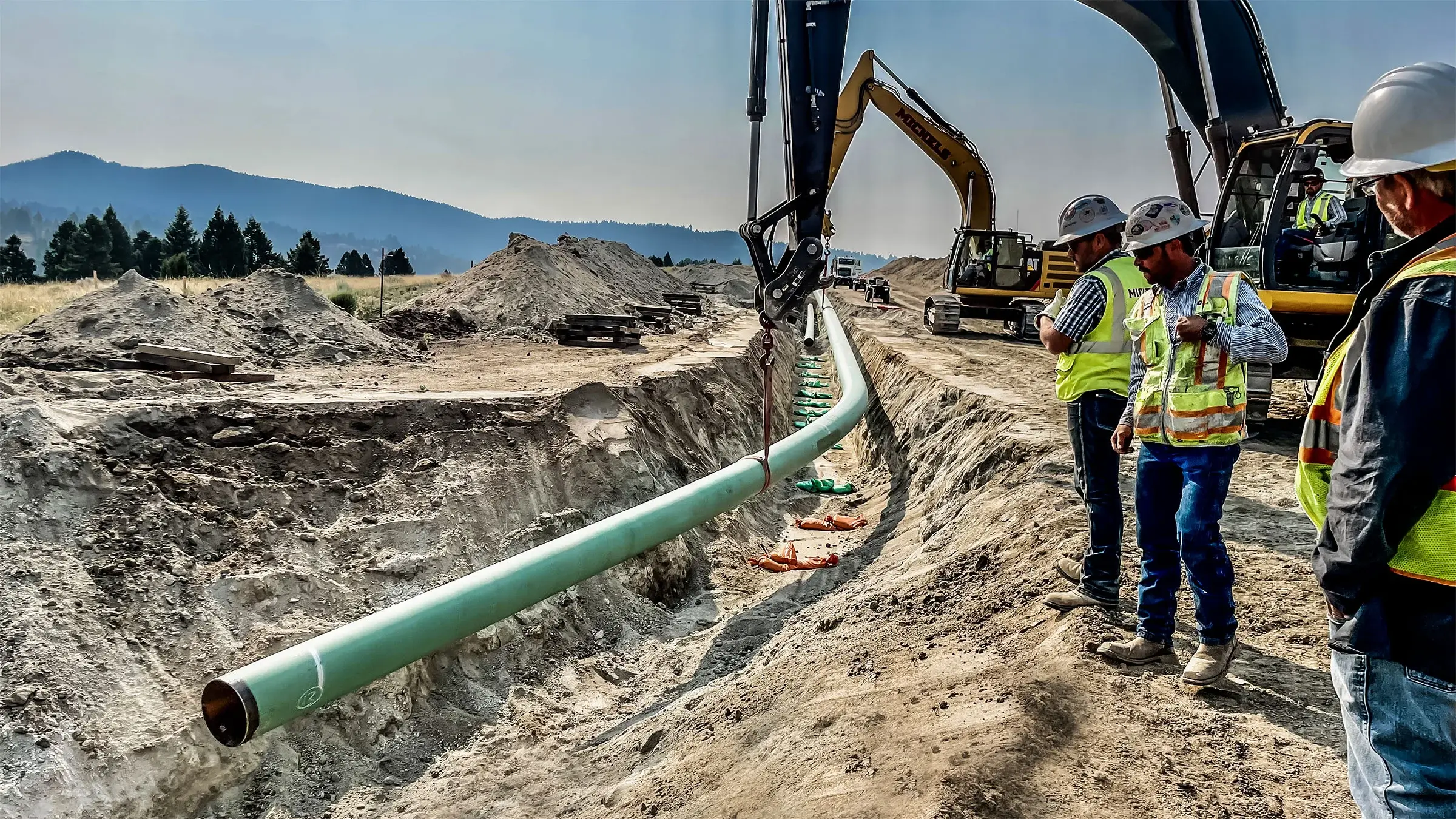 Workers assist as excavators more pipe into place