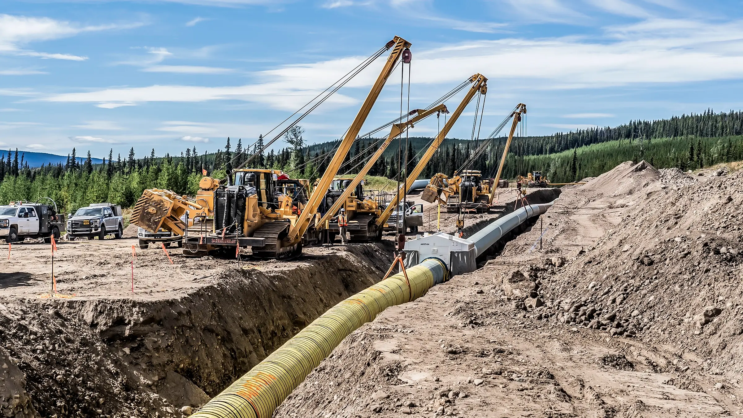 A pipeline is lowered into a trench by several pipelayers.
