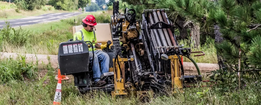 A crew member operates a cable HDD rig near a rural road.