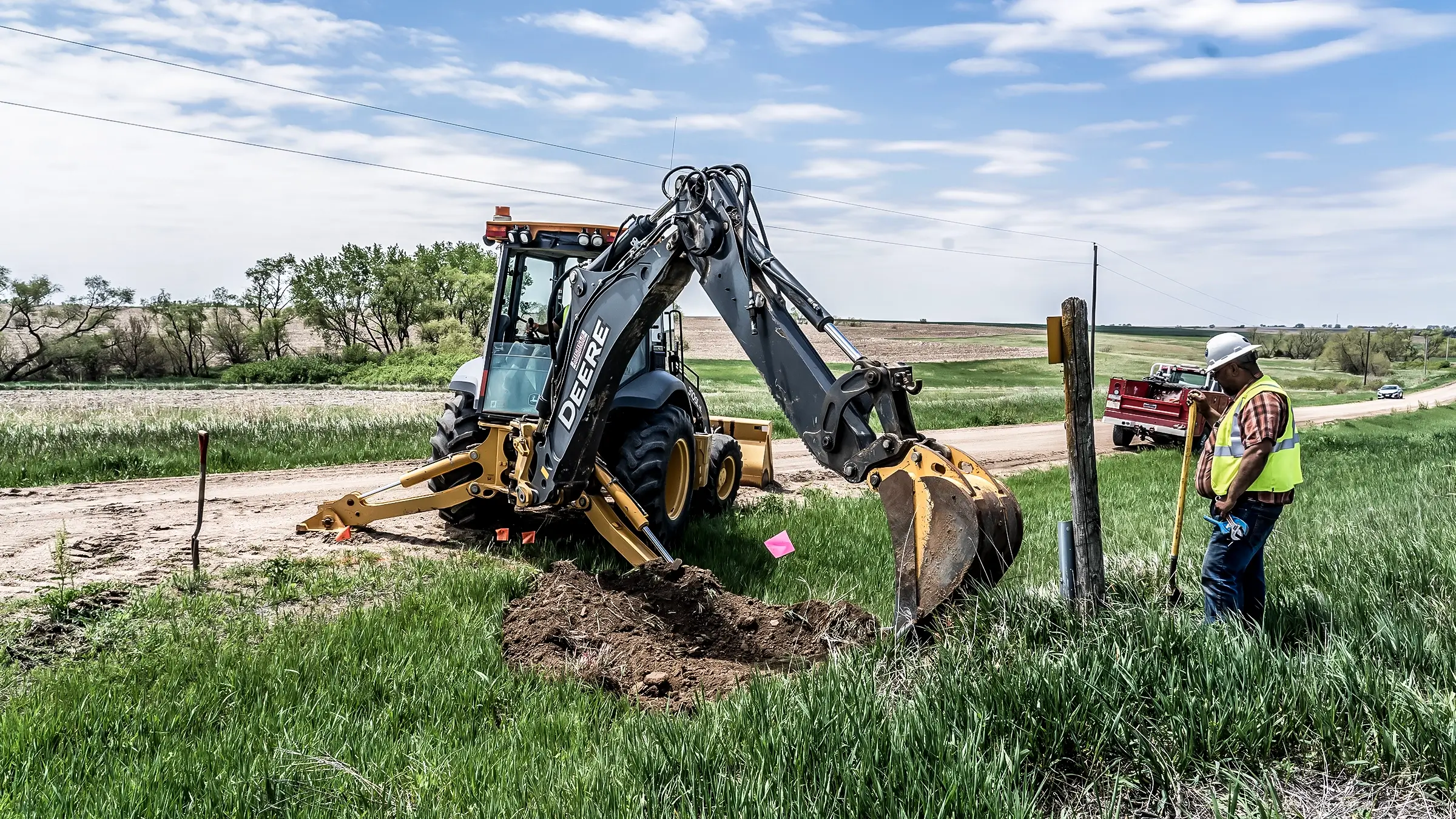 A crew member and small excavator assist in burying a cable line.