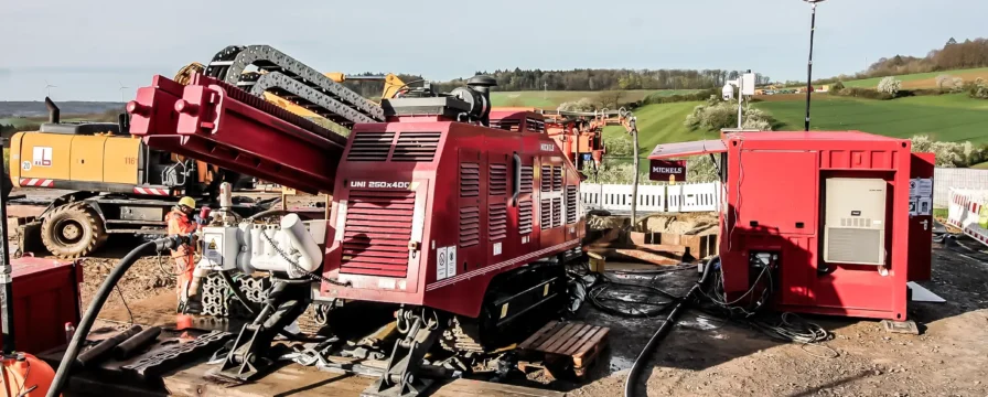 An HDD rig operating with an excavator in a rural hilly area.