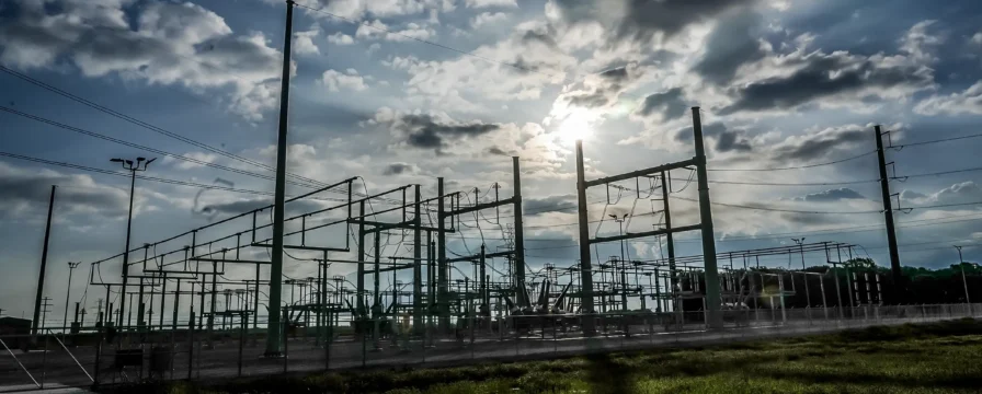 The sun shines through the clouds on a switchyard.